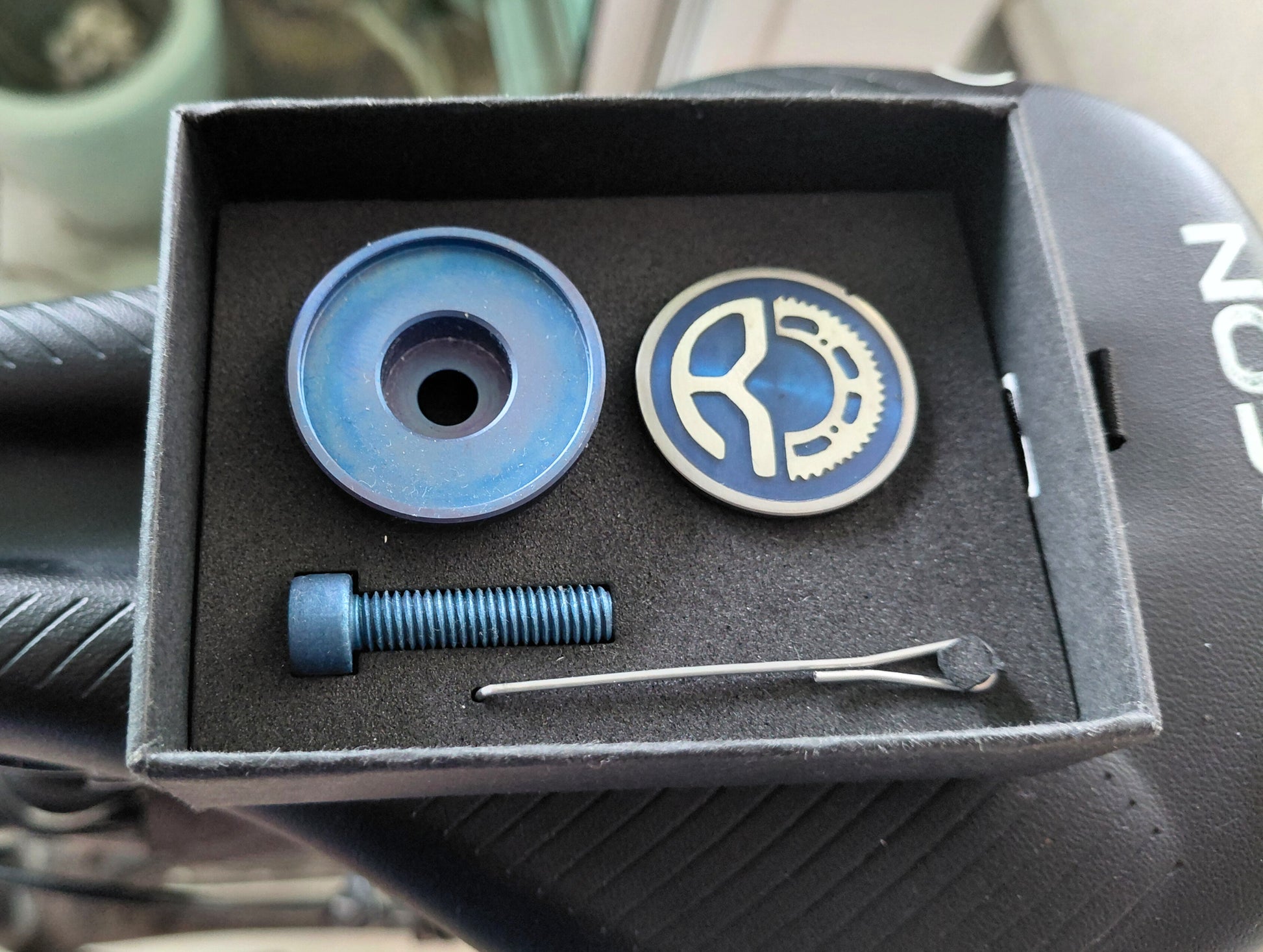 Titanium monogram stem top cap set in a gift box on a bicycle saddle.