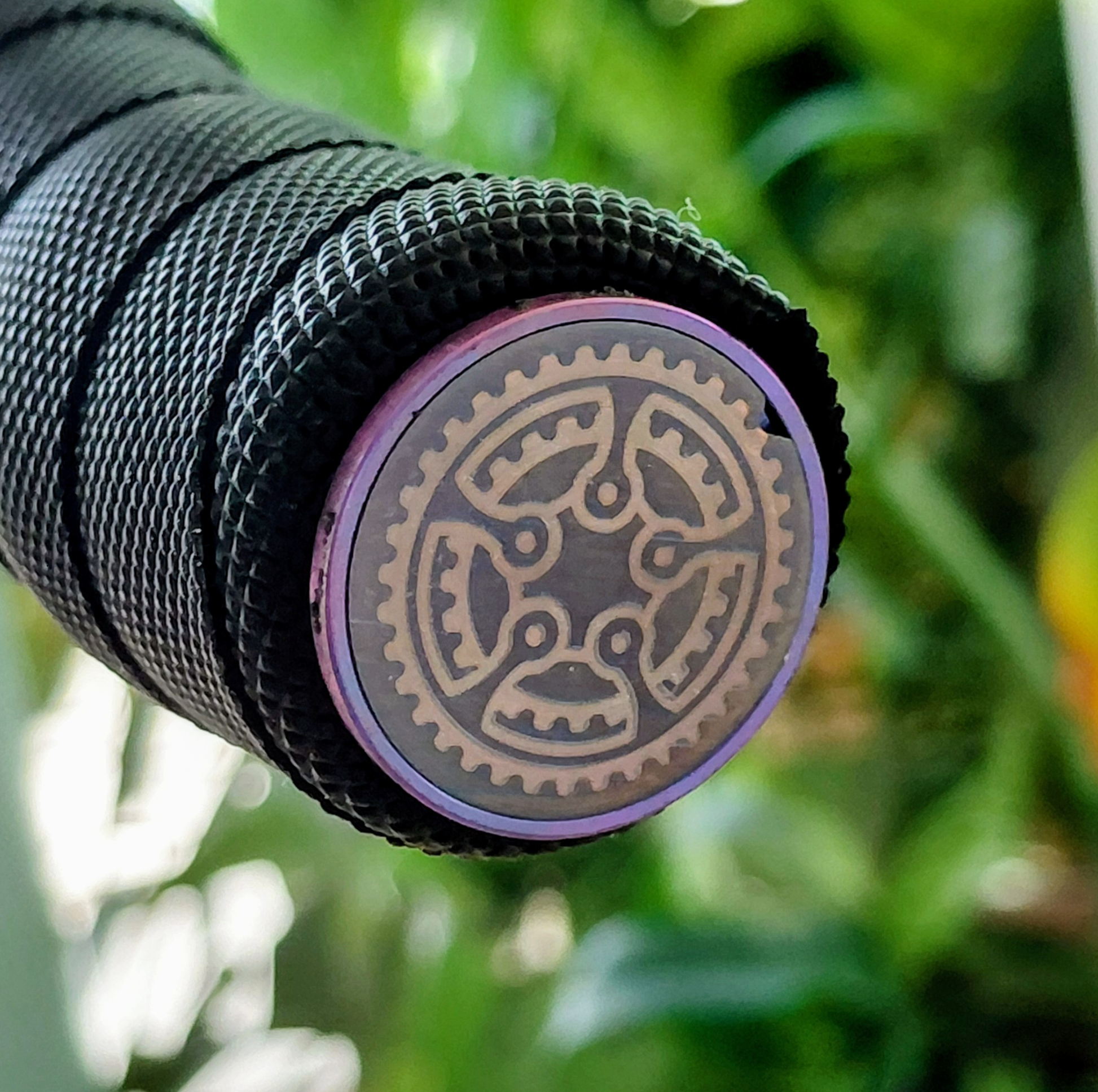 Purple and bronze titanium handle bar end cap on blurry green background