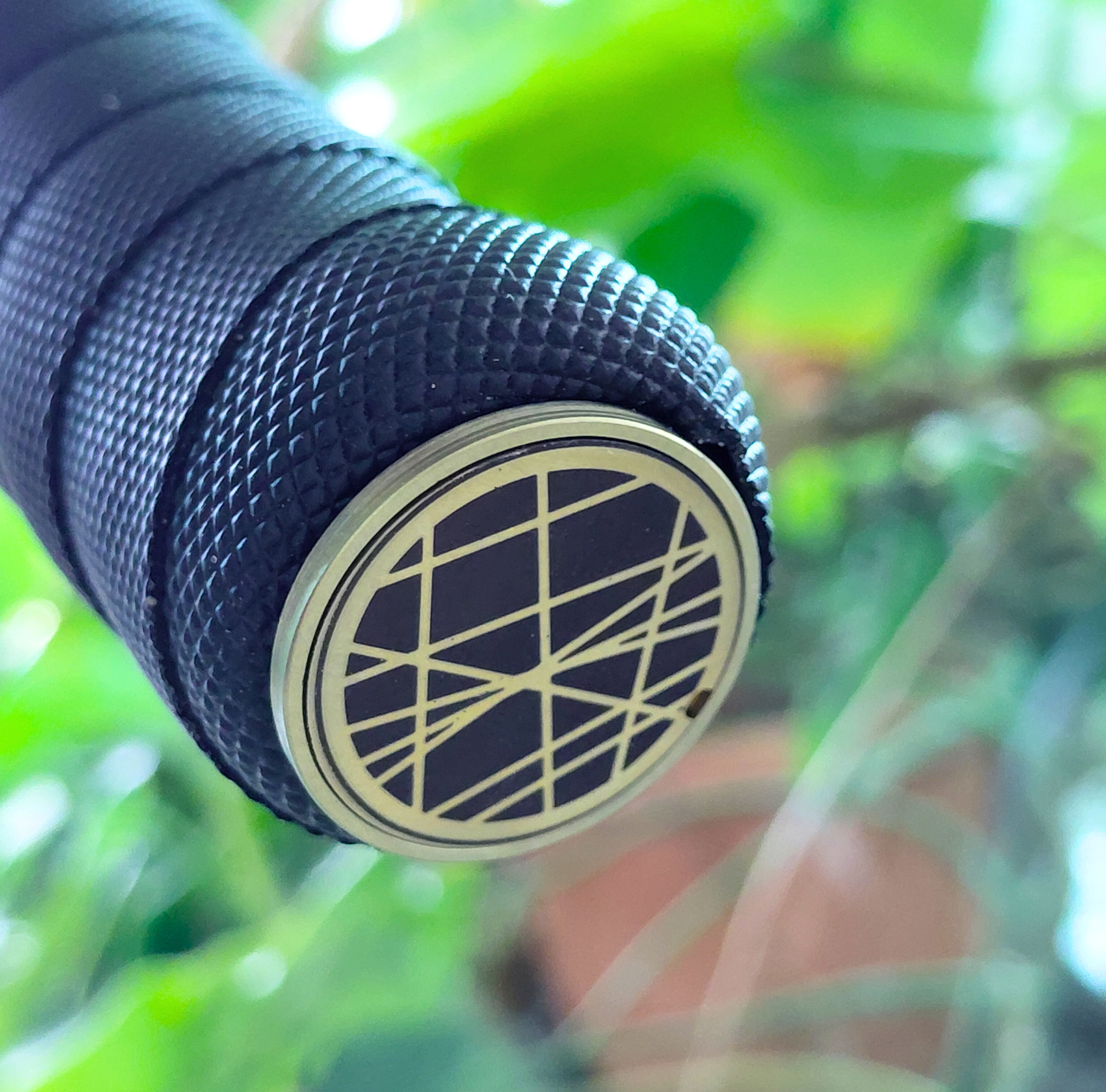 Close-up of a titanium handlebar end cap with geometric design against a blurred green background