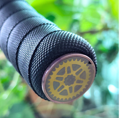 Close-up of a bicycle handlebar with a gold gear design end cap against a blurred green background