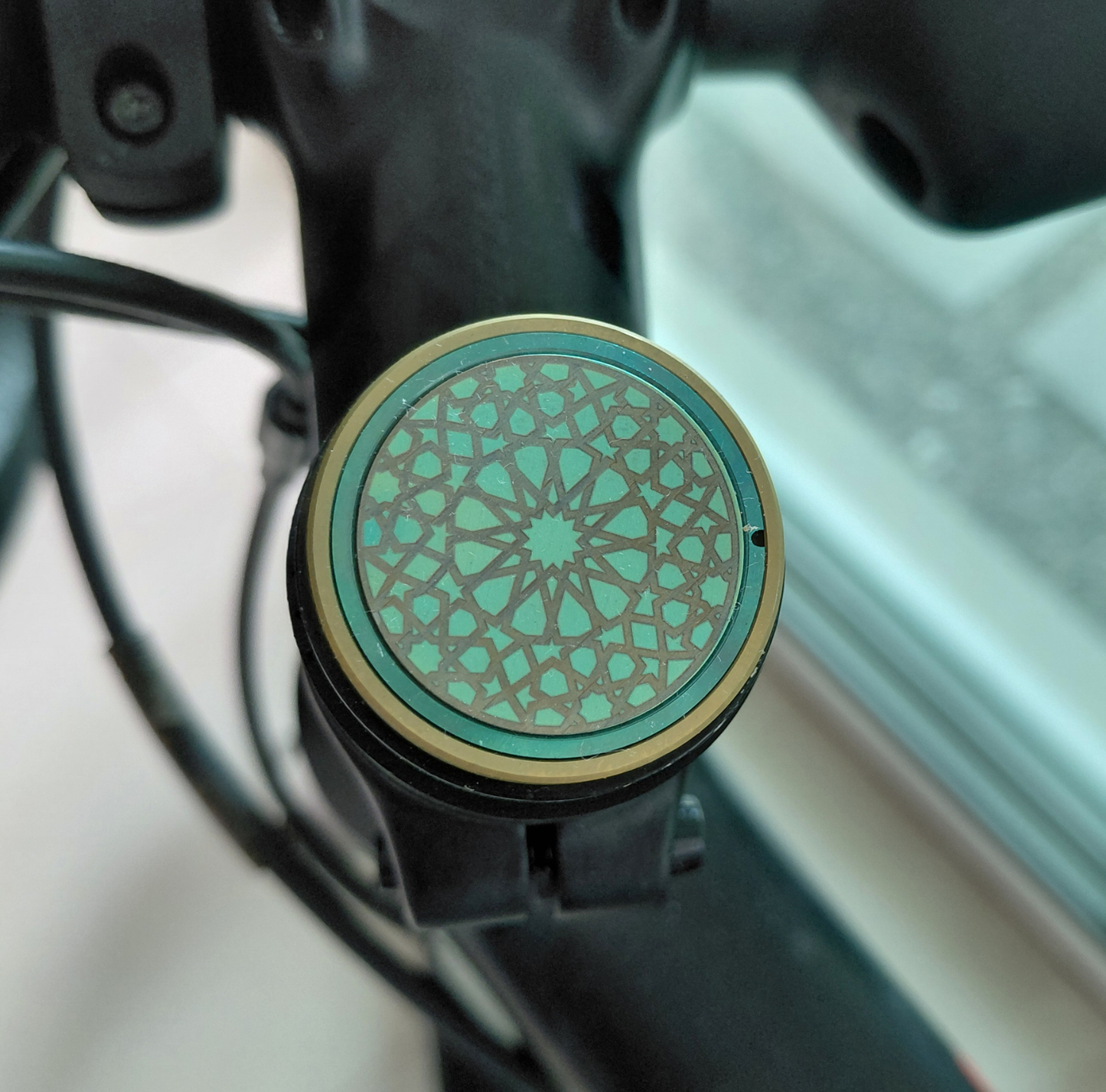 Close-up of a titanium stem cap in turquoise and gold with Islamic pattern on a blurred background 