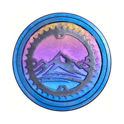 Multicoloured titanium bicycle stem top cap with mountain and chain design on a white background.